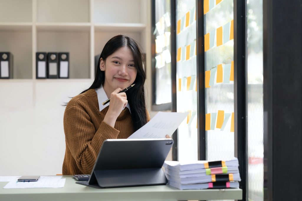 Asian Business woman using calculator and laptop for doing math finance on an office desk, tax